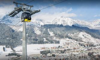 A cable car travels over a snowy mountain landscape. In the background, snow-covered mountains and the village are visible.