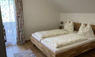 A cozy bedroom with two single beds and bright wooden details. The room has a window with curtains and a beautiful rug on the floor.
