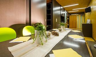 A modern designed room with a long table, decorated with plants and a runner. The room has bright walls and functional furniture, ideal for gatherings.