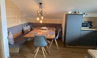 A cozy kitchen corner with a dining table and modern chairs. The walls are made of wood and there is a small kitchenette.