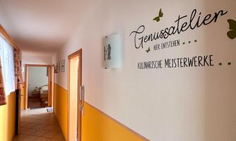 A bright hallway with orange walls and tiles. A decorative sign with the inscription "Genussatelier" hangs on the wall.
