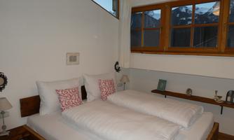 A cozy bedroom with two beds and pillows. The mountain landscape is visible through the window.