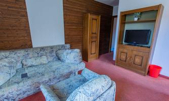 A simple living room with a comfortable sofa and an armchair. A television is on a shelf, and a bucket is visible.