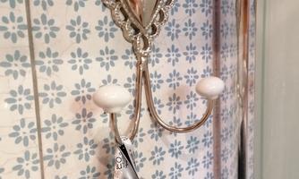 A handmade heart-shaped towel holder hangs on a tiled wall. A gray towel is attached to it.