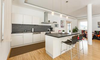 A modern kitchen with white cabinets and a cooking island. The room is bright and open with warm wooden flooring.