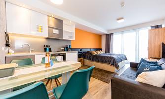 A modern living kitchen with a cozy bedroom. The room is bright and well-furnished, with large windows for plenty of daylight.