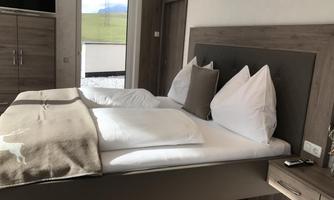 A cozy bedroom with a large bed and white pillows. The room has a modern decor and a beautiful view outside.