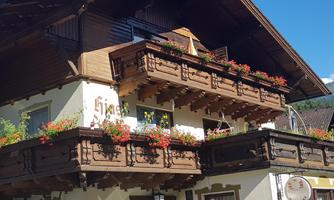 A traditional alpine house with wooden verandas and colorful flowers. The clear blue sky complements the picturesque view.
