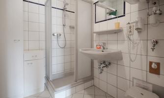 A simple bathroom area with a shower and a sink. The walls are covered with white tiles.