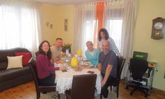 A group of five people is sitting at a table in a cozy room. There is a relaxed atmosphere with food and drinks on the table.