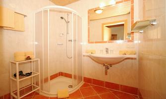 A modern bathroom with a shower and a sink. The walls are light tiled, and the floor has orange tiles.