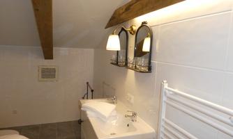 A modern bathroom with wooden details and two wall lights. The white tiles and sanitary fixtures create a bright and clean atmosphere.