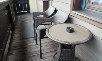 A cozy balcony with two rattan chairs and a small table. On the table, there is a cigarette box.