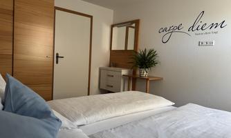 A cozy bedroom with two single beds and modern furniture. On the wall hangs the inscription "carpe diem" and there is a small plant on the table.