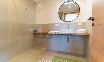 A modern bathroom with a shower and a wooden sink. The room is bright and minimally furnished.
