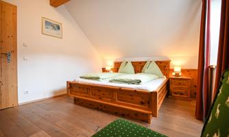 A cozy bedroom with a wooden bed and green cushions. The room has a warm atmosphere and is well-lit.