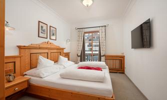 A cozy bedroom with wooden furniture and two beds.  
Large windows bring in plenty of daylight and there is a television on the wall.