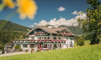A picturesque house in the mountains, surrounded by green meadows and blooming flowers. The sky is clear and the atmosphere is peaceful.