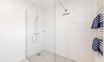 A modern shower with a glass partition and bright tiles. Fleece towels in blue are neatly placed on a towel holder.