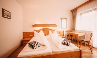 A cozy bedroom with two single beds and wooden furniture. The room has large windows with plenty of natural light.