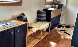 A cozy hallway with wooden flooring and modern furniture. There is a seating area with furs and decorative elements on the walls.