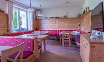 A cozy dining area with wooden furniture and pink seat covers. Large windows provide plenty of daylight.