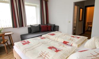 A cozy bedroom with a double bed and a sofa. Bright windows and modern colors create an inviting atmosphere.