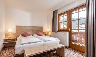 A cozy bedroom with two single beds and warm colors. The large window front offers a view outside and lets in a lot of light.