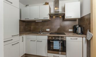 A modern kitchen with white cabinets and brown tiles. The stove, the sink, and a coffee machine are well placed.