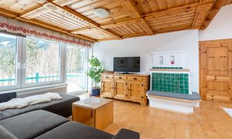 A modern living room with a wooden ceiling and large windows. There is a cozy sofa, a television, and a traditional fireplace.