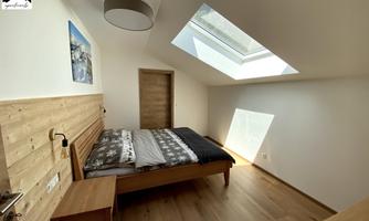 A modern bedroom with wood paneling and a large skylight. The room is bright and minimally furnished.