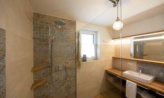 A modern bathroom with a glass shower partition and an elegant sink. The walls are designed with natural materials, and a window provides daylight.