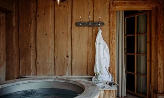A relaxing bathroom with a round hot tub and wooden paneling. A white bathrobe is hanging on the wall next to an open door.