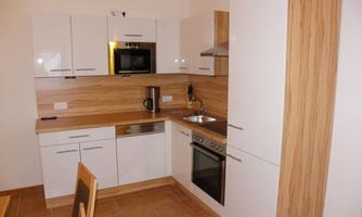 A modern kitchen with white furniture and wood accents. It is equipped with appliances such as a stove, a microwave, and a dishwasher.