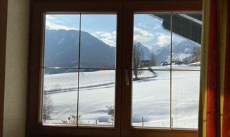 A window with views of snow-covered mountains and a clear blue sky. The landscape appears calm and idyllic.