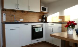 A modern kitchen with bright cabinets and wooden surfaces. On the countertop, there is a kettle and a potted plant.