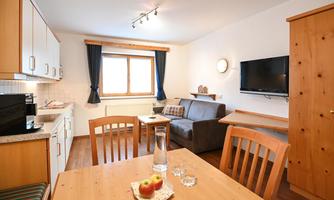 An inviting living and dining room with a modern kitchen. The space is bright and cozy, furnished with a sofa, a television, and a dining table.