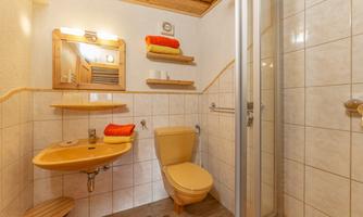 A bathroom with a shower, toilet, and a sink. The walls are tiled and there are towels in bright colors.