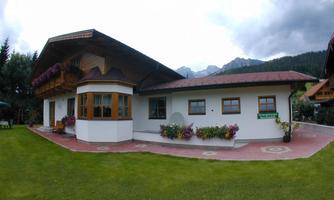 A beautiful house with a large garden and colorful flowers. In the background, mountains and a cloudy sky can be seen.