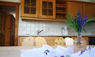 A cozy kitchen with wood-colored furniture and white tiles. On the table is a vase with purple flowers.