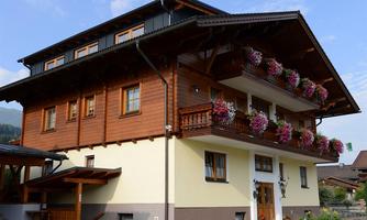 A cozy wooden house with blooming balconies. The facade is in warm colors and surrounded by a beautiful landscape.