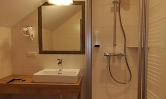 A modern bathroom with a shower and a sink. The mirror and the wooden shelf give the room a cozy atmosphere.
