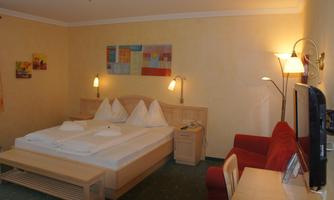 A cozy hotel room with a double bed and a red sofa. The walls are painted in soft colors and there is modern art on the walls.