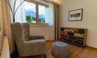A cozy room with a comfortable armchair and a small stool. Large windows offer a wonderful view of the mountains and nature.