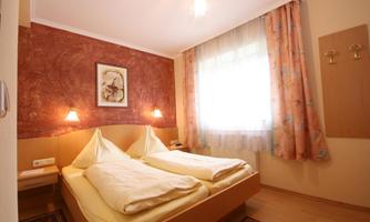 A cozy bedroom with two single beds and warm colors. The room is well-lit with a large window and friendly decoration.