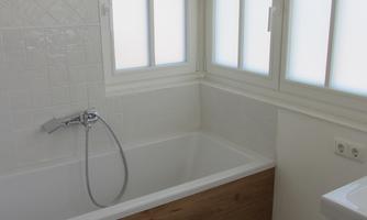 A modern bathroom with a bathtub and a toilet. There are large windows that let in a lot of light.