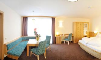 A cozy hotel room with two beds and a seating area. Large windows provide plenty of daylight.