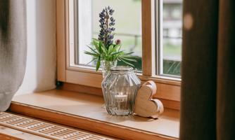 A decorative windowsill with a flower in a glass vase and a wooden heart. The warm atmosphere is enhanced by the light falling through the window.