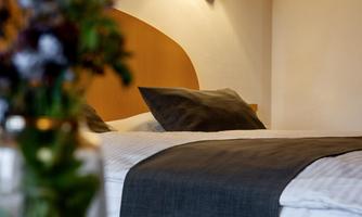 A cozy hotel room with a large bed and a bedside table. In the foreground, there is a vase with colorful flowers.