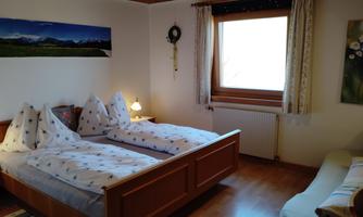 A cozy bedroom with two single beds and a bright window front. The walls are simply designed, and there is a small seating area.